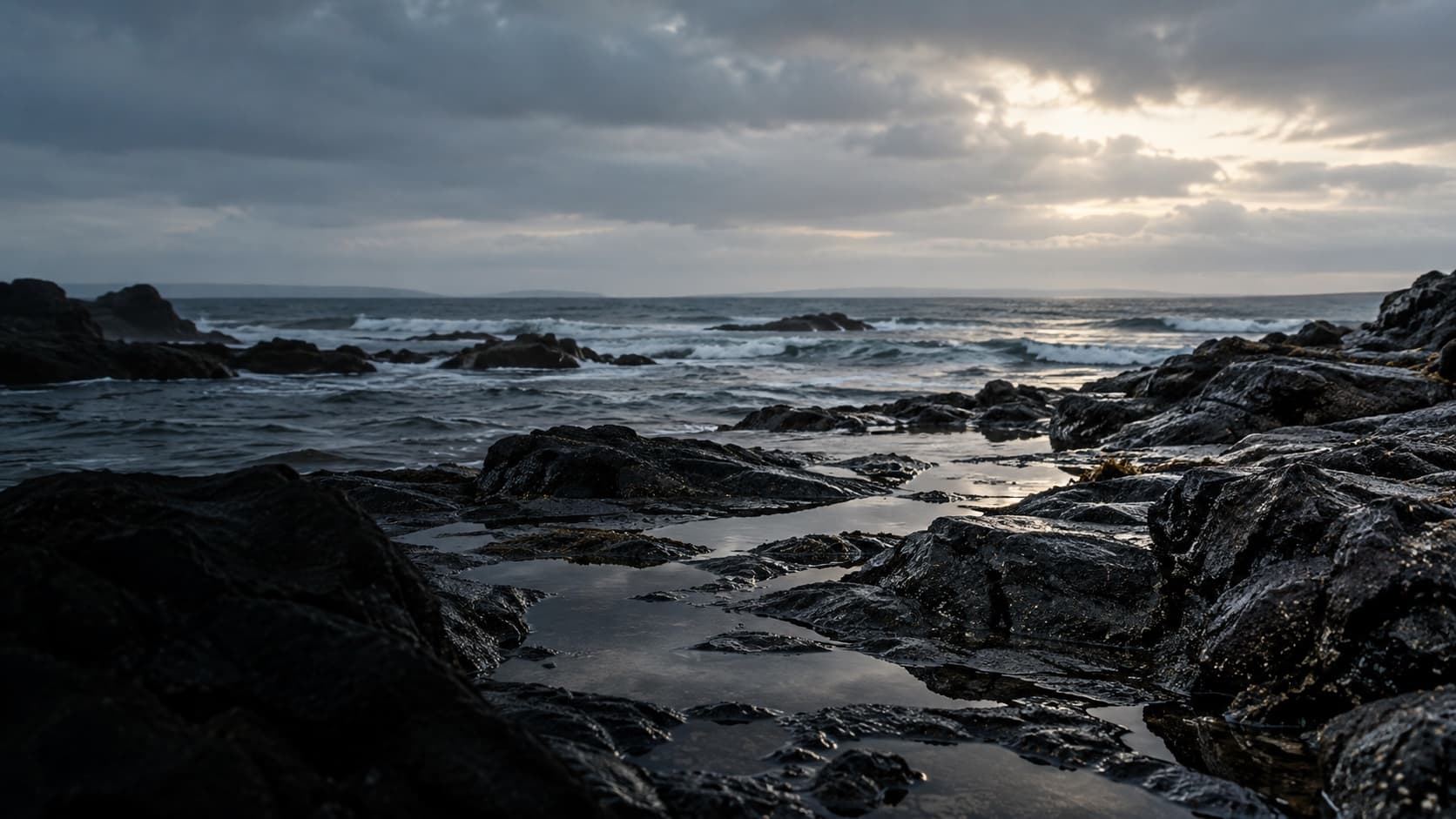 A low Atlantic tide crossing dark basalt rock beneath a wide, open sky